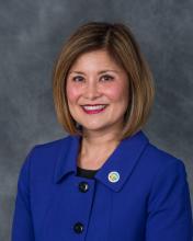 Susan Shin Angulo smiling in blue suit with gray background