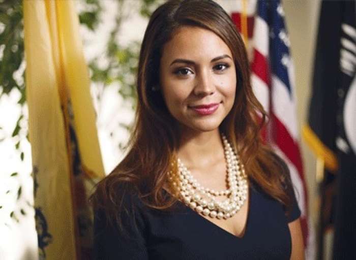 Maria in a navy blue blouse in front of an american flag