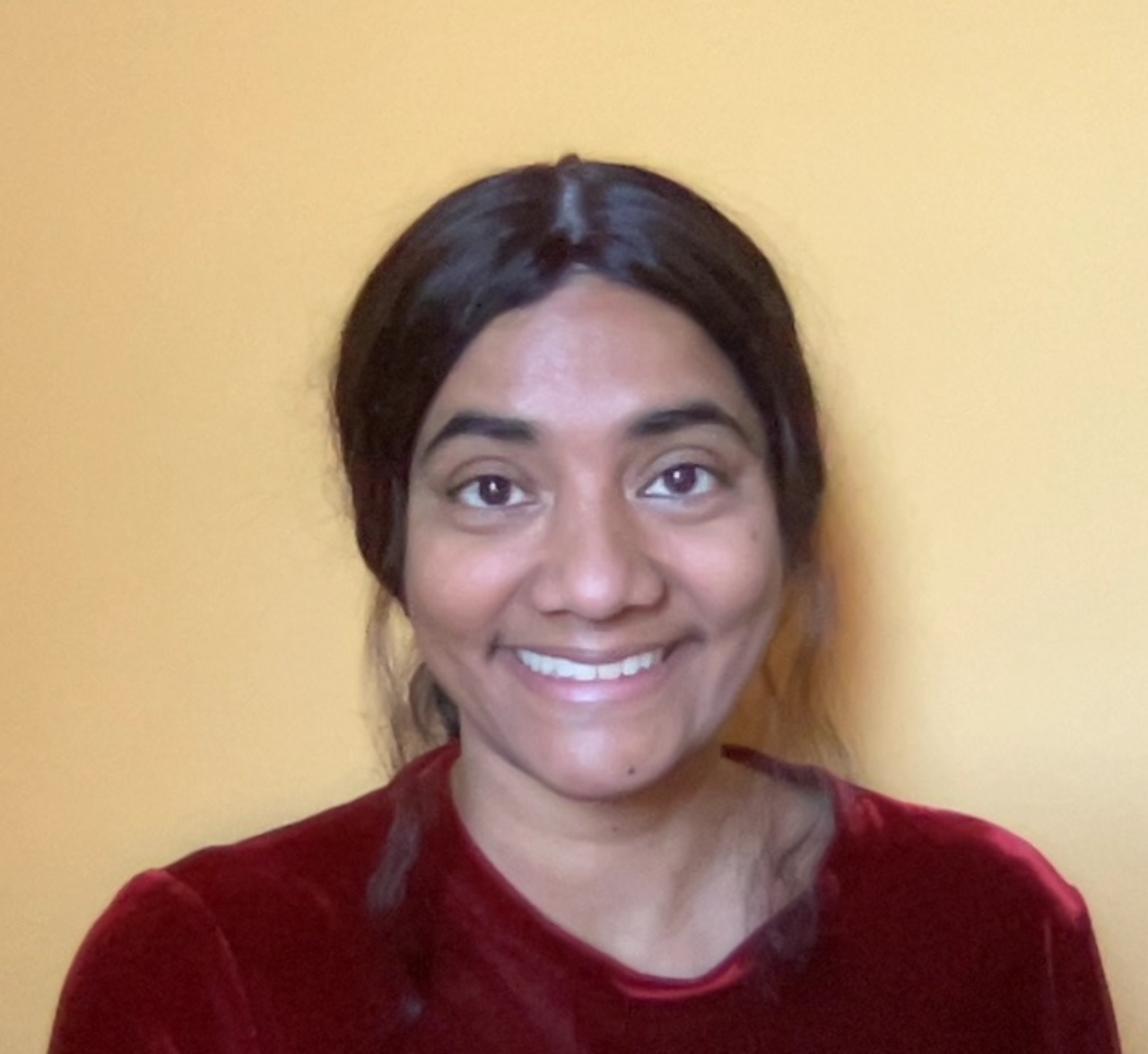 Kani Ilangovan in a red blouse in front of an off-white background