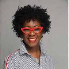 Marilyn Davis in a striped shirt and red glasses in front of a gray background