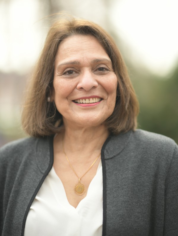 Shama Haider in a grey blazer with a white top in front of a blurred background