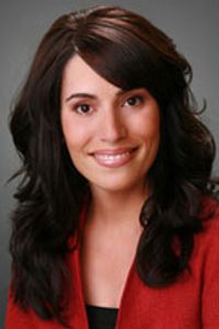 Teresa Ruiz in a red blazer in front of a gray background