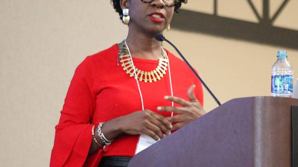 Woman in red blouse and black skirt standing behind wooden podium