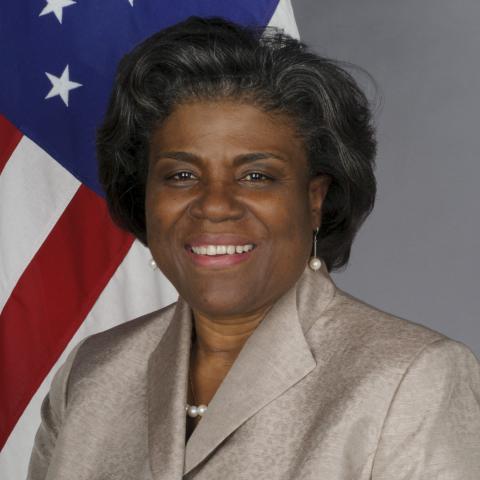 Linda Thomas Greenfield smiling in front of American flag in beige suit jacket