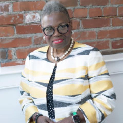 Head shot of Jeannine LaRue wearing yellow and white striped jacket, standing against brick background