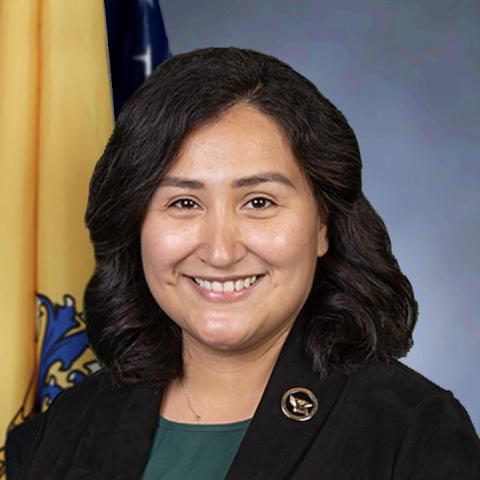 Head shot of Josely Castro wearing a black jacket and green shirt against a yellow and blue backdrop 