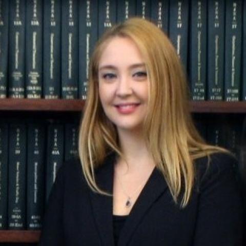 Head shot of Lauren Zyriek Enriquez wearing a black jacket against a bookshelf background