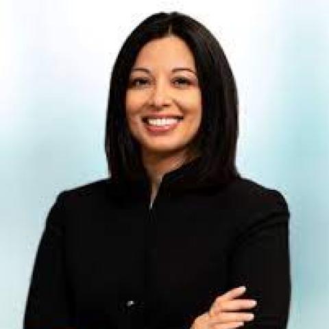 Head shot of Sapana Shah wearing a black jacket and standing against a blue background