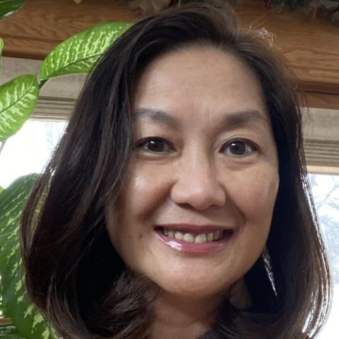 Head shot of Thuy Anh Le wearing a peach shirt with a green plant in the background