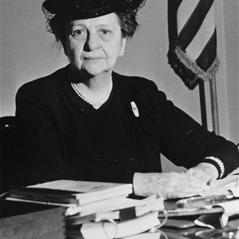 Frances Perkins sitting on a table with books/documents.