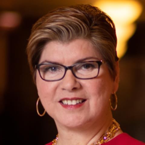 Head shot of Nellie Pou with glasses wearing a red jacket, gold necklace and hoop earrings