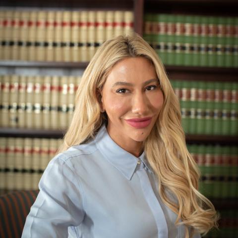 Head shot of Sarah Neibart wearing a blue shirt with a bookcase in the background