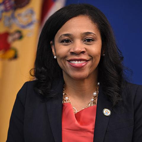 Tahesha Way smiles in front of the New Jersey state flag