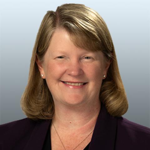 Christine Shipley's headshot. She's smiling at the camera wearing a dark colored top against a light blue background