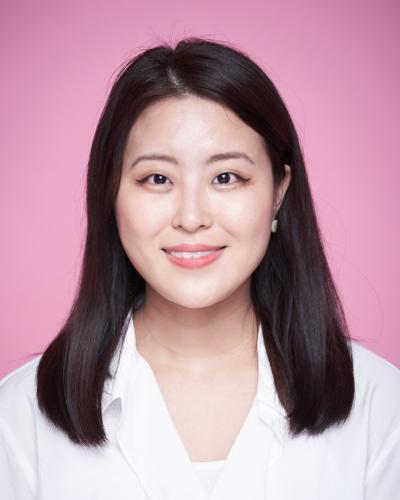 Cana Kim in a white blouse in front of a pink background