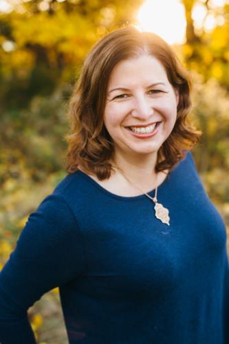 Heather Silber Mohamed in front of a blurred outdoor background in a blue blouse