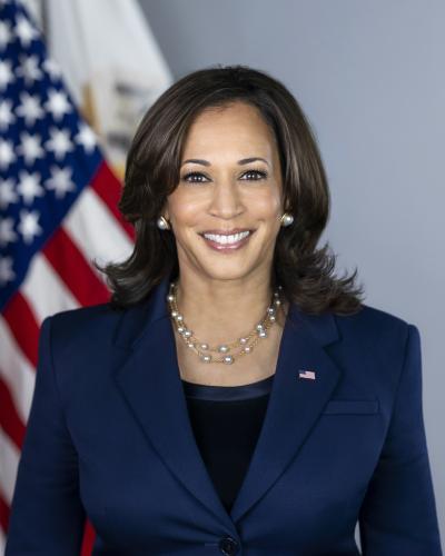 Kamala Harris smiling in dark suit with American flag to her left