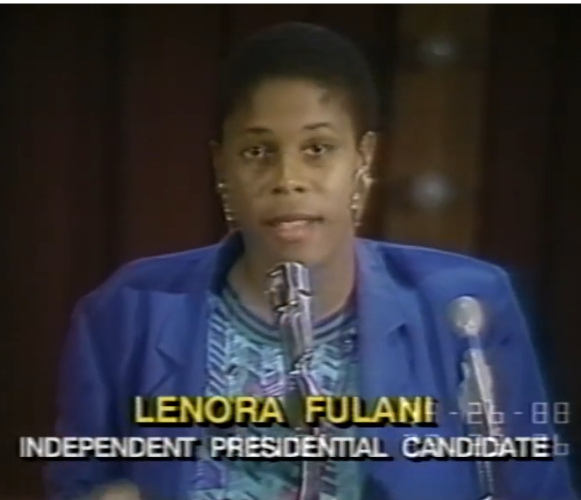 Lenora Fulani, Independent Presidential Candidate, wearing a blue suit against black background, microphone to the right. 