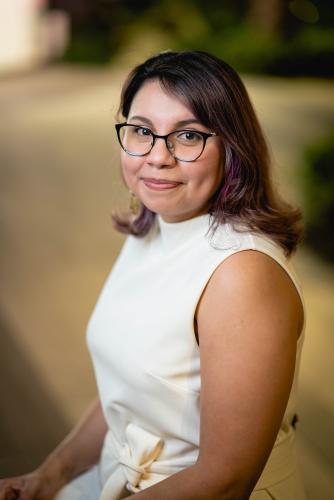 Maricruz sitting in a white dress in front of a blurred background