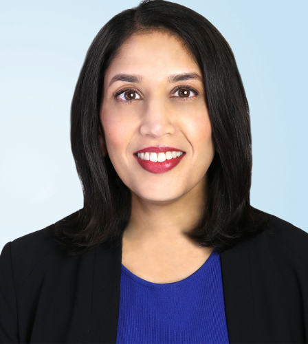 Sameena Mustada in a blue blouse and black blazer in front of a light blue background