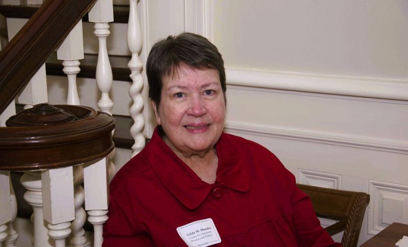 Gilda Morales seated by stair bannister, with short brown hair and wearing a red collared jacket