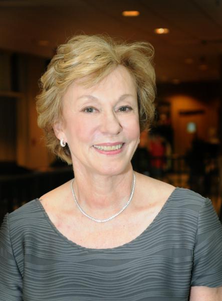 Woman with short blond hair wearing a gray blouse and silver necklace