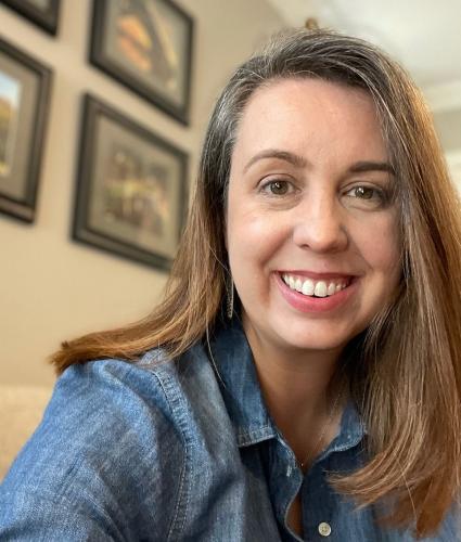 Emily Farris in a chambray shirt in front of a wall with picture frames