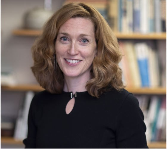 Jill Greenlee in a black shirt in front of a blurry background of a bookshelf