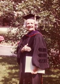 Katherine Neuberger as an adult wearing a doctorate cap and gown