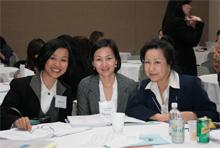 Three Asian American women dressed in business attire sitting at a round table.