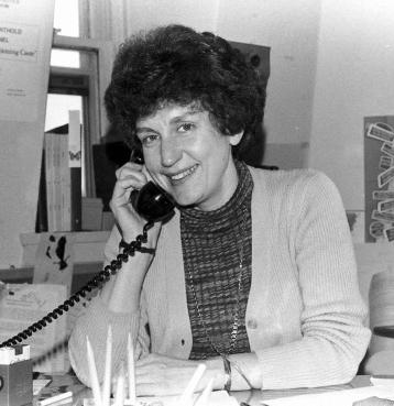A young Ruth sitting at a desk and smiling with a corded phone to her ear