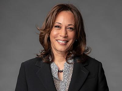 Vice President Kamala Harris smiles in black suit jacket and white top with black dots