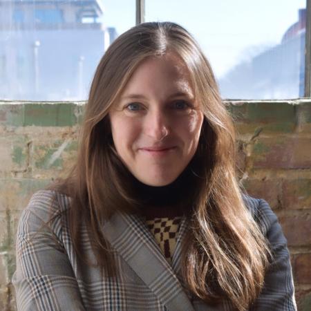 Alex Snipes in patterned blazer smiling in front of brick background
