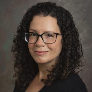 Erin Cassese in a black blouse in front of a gray background