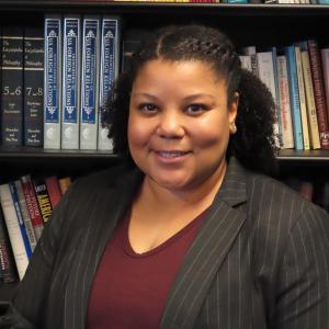 Rana McReynold in blazer and red blouse in front of bookcare