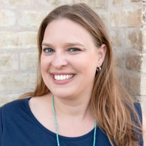 Heather Ondercin in a blue blouse in front of a white brick wall