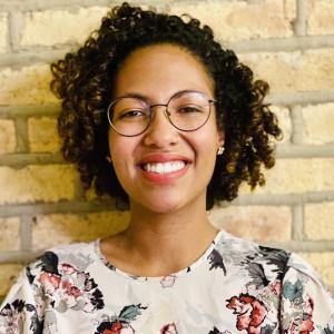 Michelle Bueno Vásquez wearing floral shirt smiling against brick wall