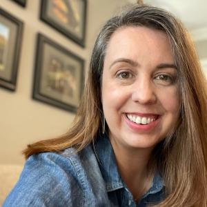 Emily Farris in a chambray shirt in front of a wall with picture frames