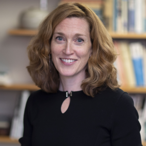 Jill Greenlee in a black shirt in front of a blurry background of a bookshelf