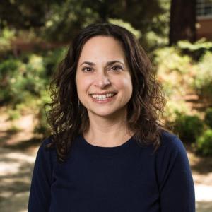 Jennifer Merolla in a navy blue shirt in front of a blurry background of greenery