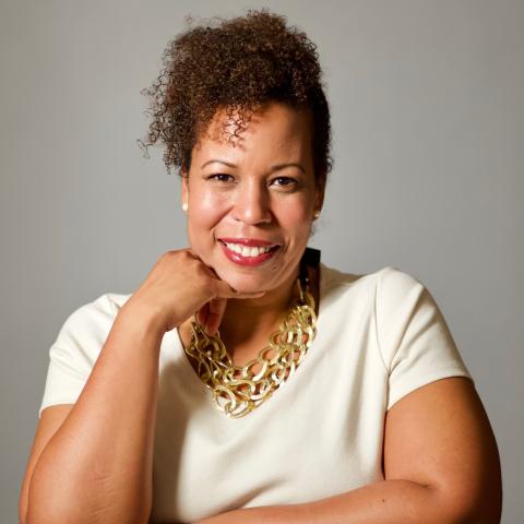 Head shot of Kimberly Peeler-Allen wearing white shirt and gold necklace against a gray background